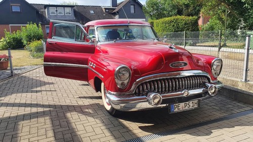 A shiny red vintage car with chrome details parked on a street on a sunny day, classic car, Buick