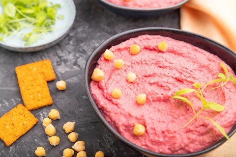Hummus with beet and microgreen basil sprouts in ceramic bowl on a black concrete background and