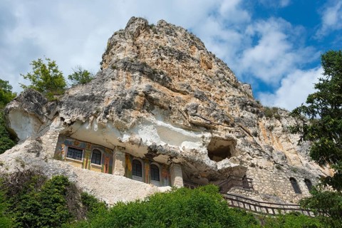 Historic cave church built into a steep rock under a clear blue sky, Bulgarian Orthodox cave