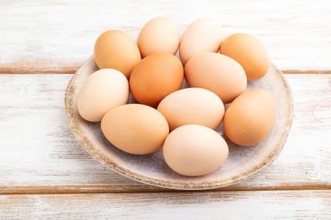 Pile of colored chicken eggs on plate on a white wooden background. side view, close up