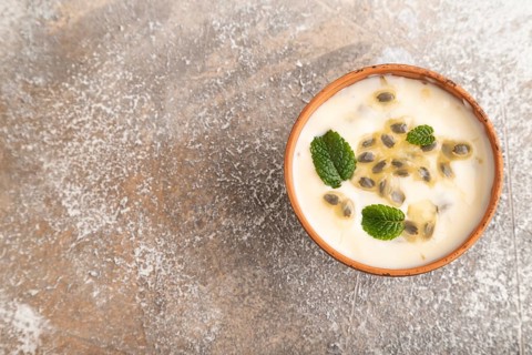 Yoghurt with granadilla and mint in clay bowl on brown concrete background. top view, flat lay,