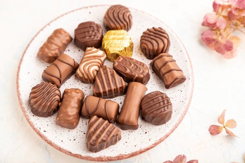 Chocolate candies with cup of coffee and hydrangea flowers on a white concrete background. side