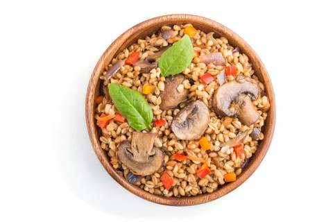 Spelt (dinkel wheat) porridge with vegetables and mushrooms in wooden bowl isolated on white