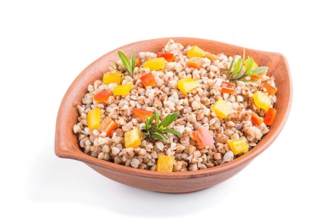 Buckwheat porridge with vegetables in clay bowl isolated on white background. Side view, close up.