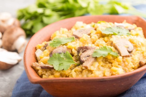 Lentils porridge with champignons and coriander in a clay bowl on a gray concrete background and