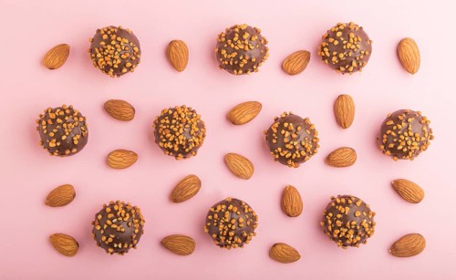 Chocolate caramel ball candies with almonds in a row on a pastel pink background. top view, flat