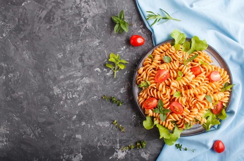 Fusilli pasta with tomato sauce, cherry tomatoes, lettuce and herbs on a black concrete background