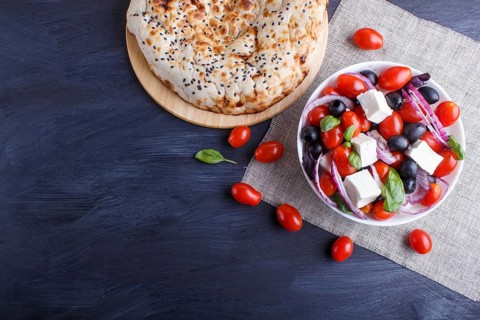 Greek salad with fresh cherry tomatoes, feta cheese, black olives, basil and onion on black wooden
