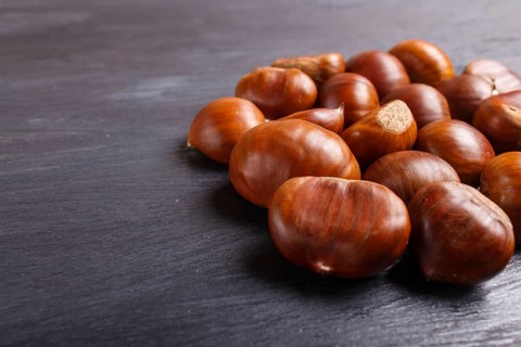 Pile of sweet chestnuts on black wooden background with copy space, top view