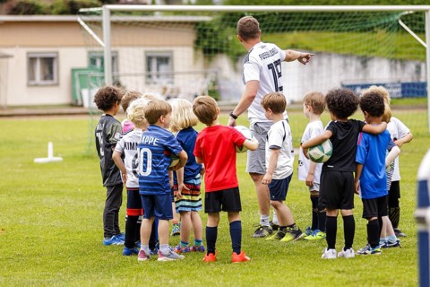 Volunteer coach trains children on the football pitch, Bonn, 19.06.2024