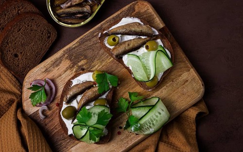 Sandwiches, black bread with sprats, cream cheese, cucumbers, on a cutting board, top view,