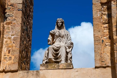 Stone figure of a historical figure in a stone frame in front of a clear blue sky, Teatro Romano de