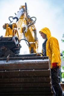 Construction worker in yellow rain jacket working with large construction machine in the rain,