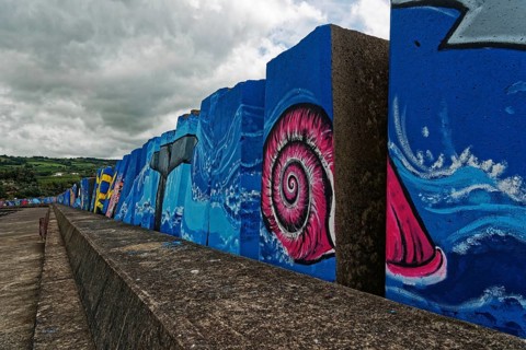 Colourful mural by the sea with a large pink snail under a cloudy sky, small town of Vila Franca do