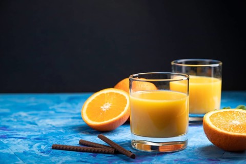 Glass of orange juice on a black and blue background. Hard light, contrast. Side view, copy space