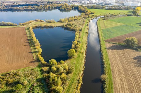 River Leine meanders through farmland and meadows, sugar factory of company Nordzucker in the back,