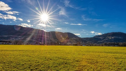Bright sun over a green meadow in front of a mountain range in a clear sky, Bad Feilnbach