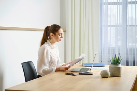 A focused professional woman realtor is reviewing a paper document at her clean, organized