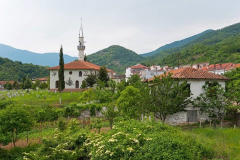 Rural scene with mosque and minaret in the foreground, surrounded by lush vegetation and mountains,