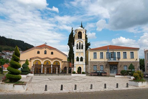 A classical church with a bell tower stands in a paved square under a cloudy sky, Xanthi, Eastern