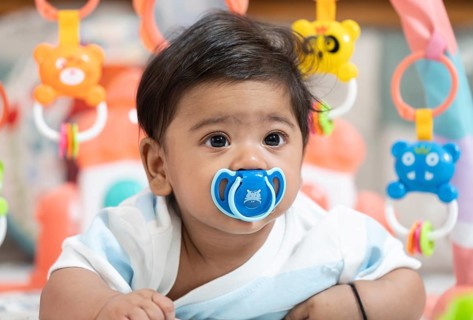 Baby boy playing lying on bed with pacifier on mouth