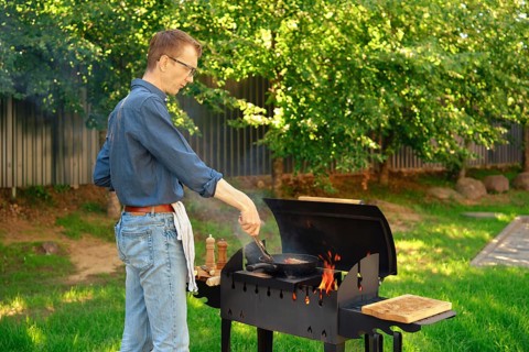 Middle-aged man puts a steak on a frying pan with kitchen tongs while making food at backyard