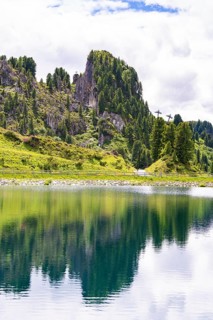 A clear mountain lake reflects the surrounding trees and mountains under a cloudy sky, Penken,