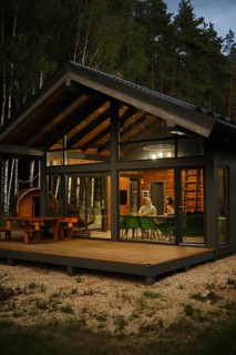 A view from outside at the couple sitting behind dining table in modern forest cabin in the evening