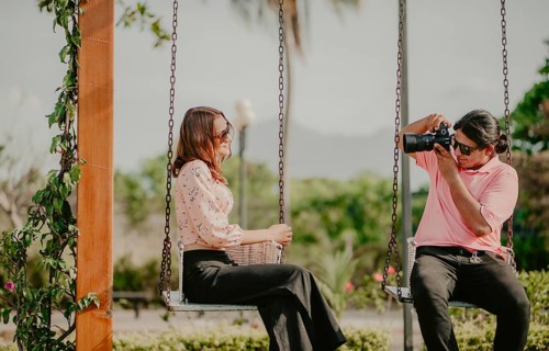 Boyfriend taking a photo of his girlfriend on a swing in a park. Boyfriend photographing girlfriend