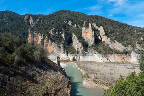 A river flows through a rocky landscape surrounded by high, steep cliffs and wooded mountains under