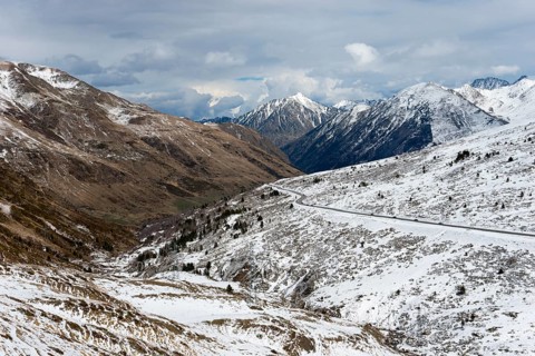 Schneebedeckte Berge und ein kurvenreiches Tal in Andorra, durchzogen von einer Straße, nördlich