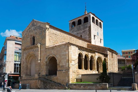 Romanesque church with high tower and arches, built of stone, under a blue sky in sunny weather,