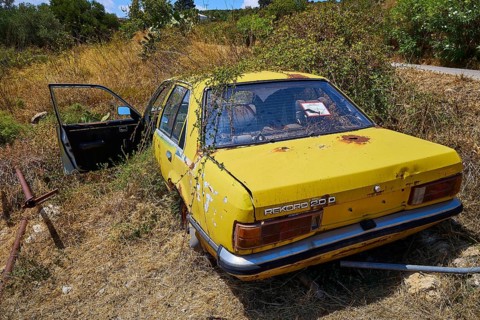 Yellow, old car left behind, overgrown with weeds in summer weather, wrecked vehicle, Crete, Greek