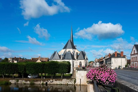 Kirche in einem kleinen Dorf mit klarblauem Himmel und grünen Bäumen, Blumen auf einer Brücke und