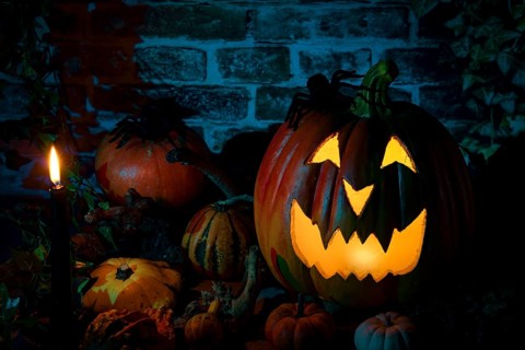 Glowing Halloween pumpkin, surrounded by a candle and various decorative pumpkins