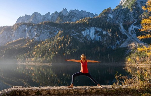 A woman doing yoga by the lake. Warrior 2 (Virabhadrasana) . Vorderer Gosausee in autumn with a