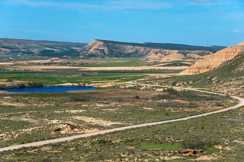 Landscape with fields, hills and a lake under a clear blue sky, Bardenas Reales Natural Park,