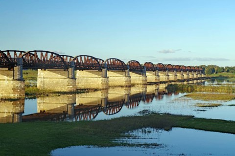 Long stone bridge with many arches crossing a calmly reflecting river, surrounded by nature,