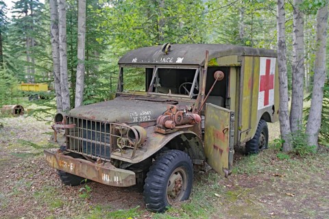 Rusty, old army ambulance, with Red Cross symbol between trees in the forest, former army camp,