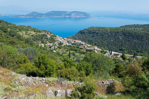 Coastal landscape with a village surrounded by green hills and the blue sea in the background,