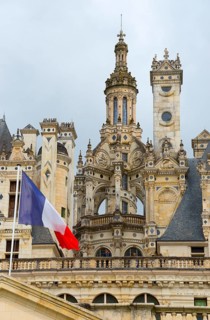 Detailed view of a historic castle with elaborate decorations and a French flag in the foreground,