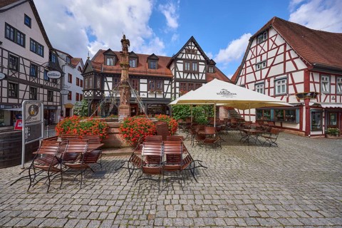 Market fountain with geraniums, half-timbered houses and outdoor areas of a restaurant with