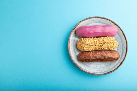 Set of eclair, traditional french dessert on ceramic plate on blue pastel background. top view,