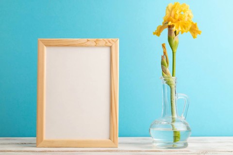 Wooden frame with yellow iris flower in glass on blue pastel background. side view, copy space,
