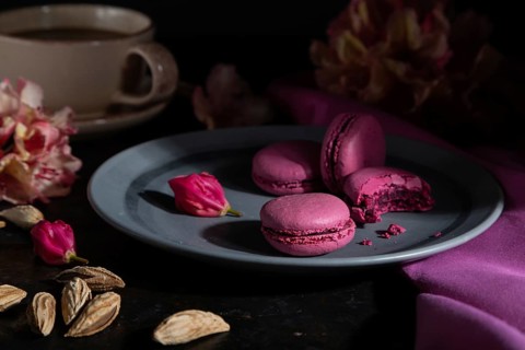 Purple macarons or macaroons cakes with cup of coffee on a black concrete background and pink