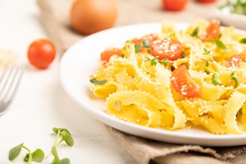 Reginelle semolina pasta with tomato, eggs, sesame and microgreen sprouts on a white wooden