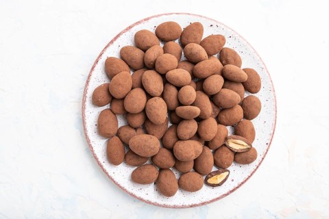 Almond in chocolate dragees on ceramic plate on white concrete background. Top view, close up, flat