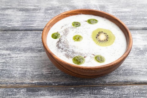 Yogurt with kiwi, gooseberry, chia and almonds in wooden bowl on gray wooden background. side view,
