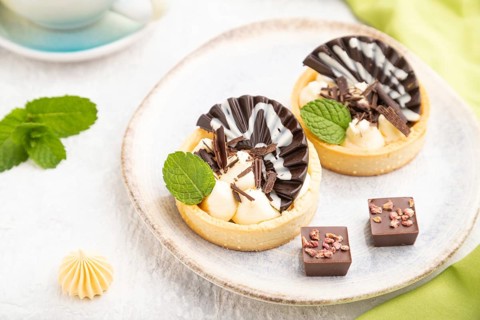 Sweet tartlets with chocolate and cheese cream with cup of coffee on a gray concrete background and