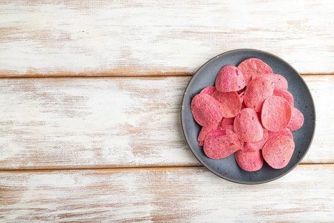 Red potato chips with herbs and tomatoes on white wooden background. Top view, flat lay, copy space
